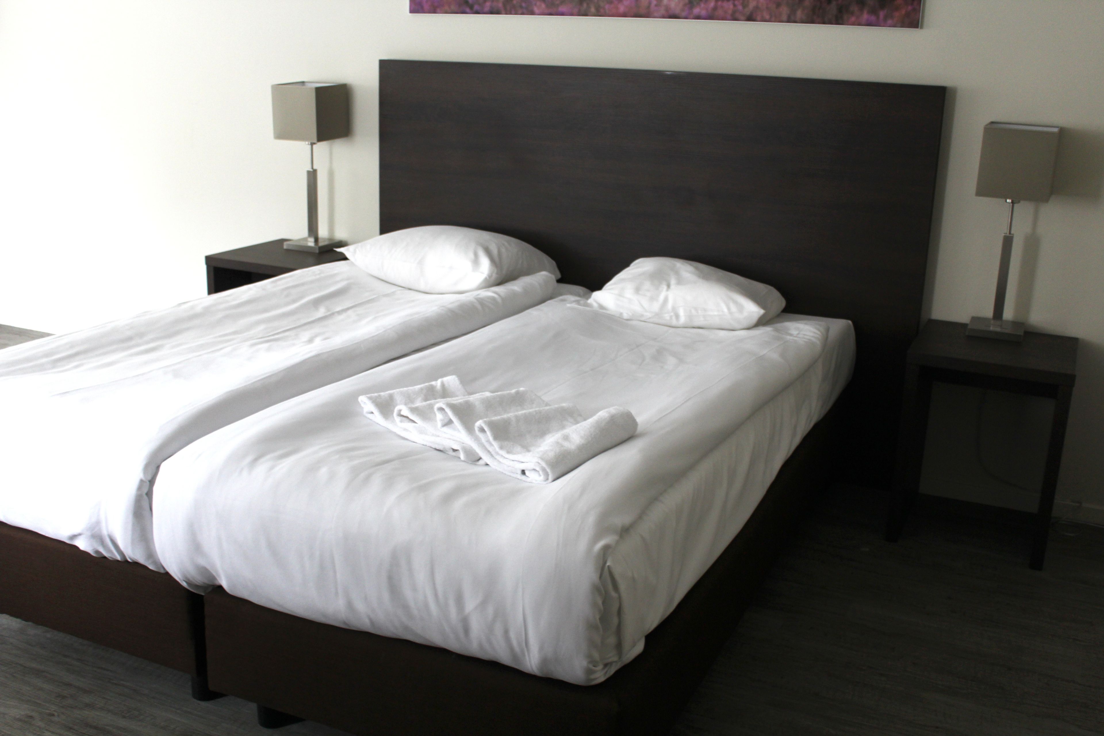 A double bed with white linens and two bedside tables with lamps.