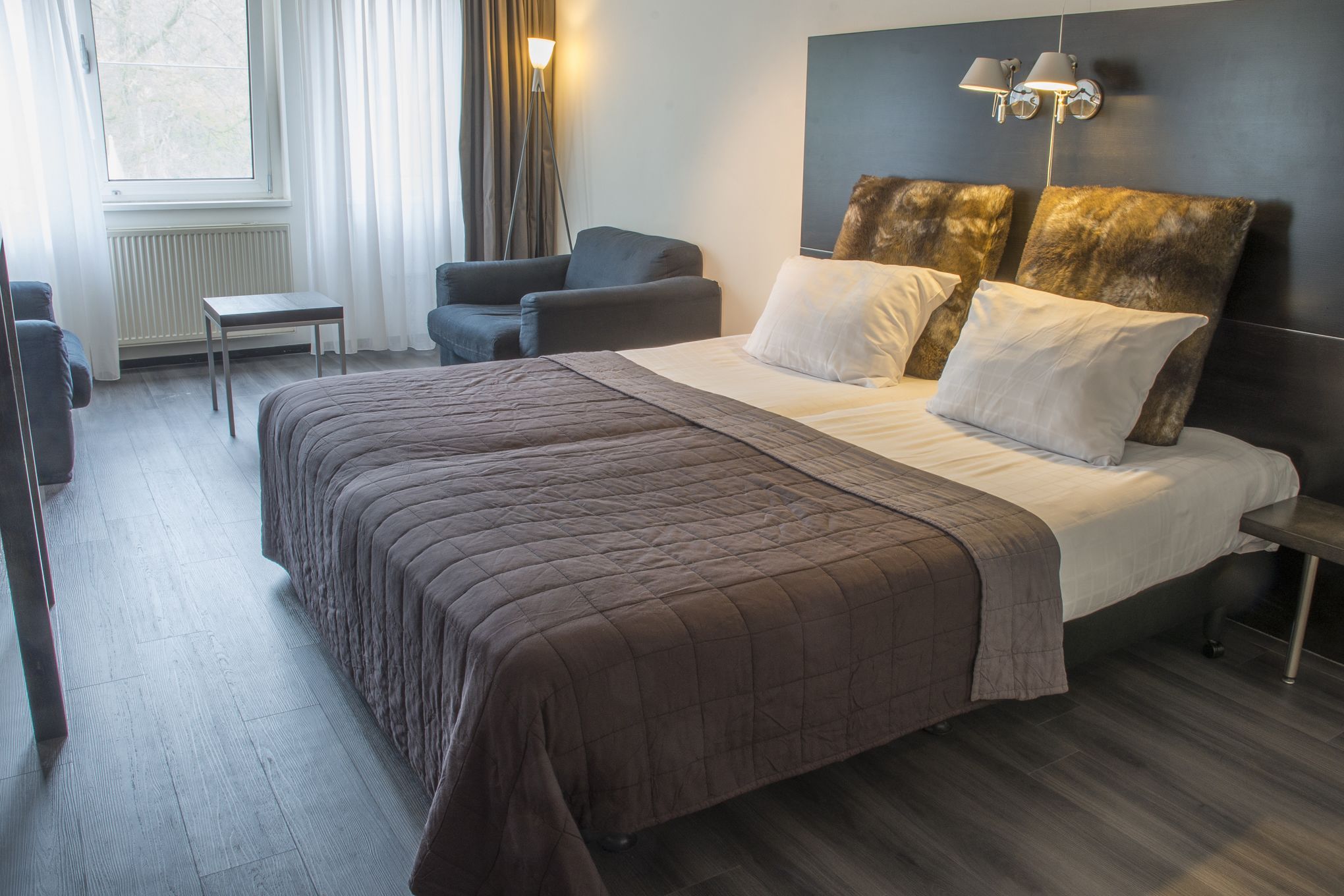 A hotel room with a large bed, a desk, a chair, and a window with curtains.