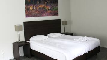 A neatly made bed with white linens, two bedside tables with lamps, and a painting of deer on the wall.