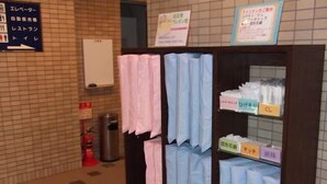 Baño con señalización para personas mayores, un extintor y un estante con toallas y artículos de aseo.