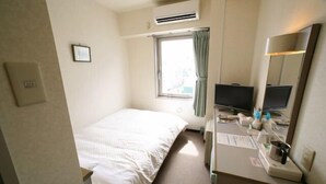 Habitación de hotel con cama, escritorio con computadora y espejo, ventana con cortinas y un equipo de aire acondicionado.