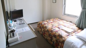 Habitación de hotel con cama, escritorio con computadora, ventana con cortinas y aire acondicionado.