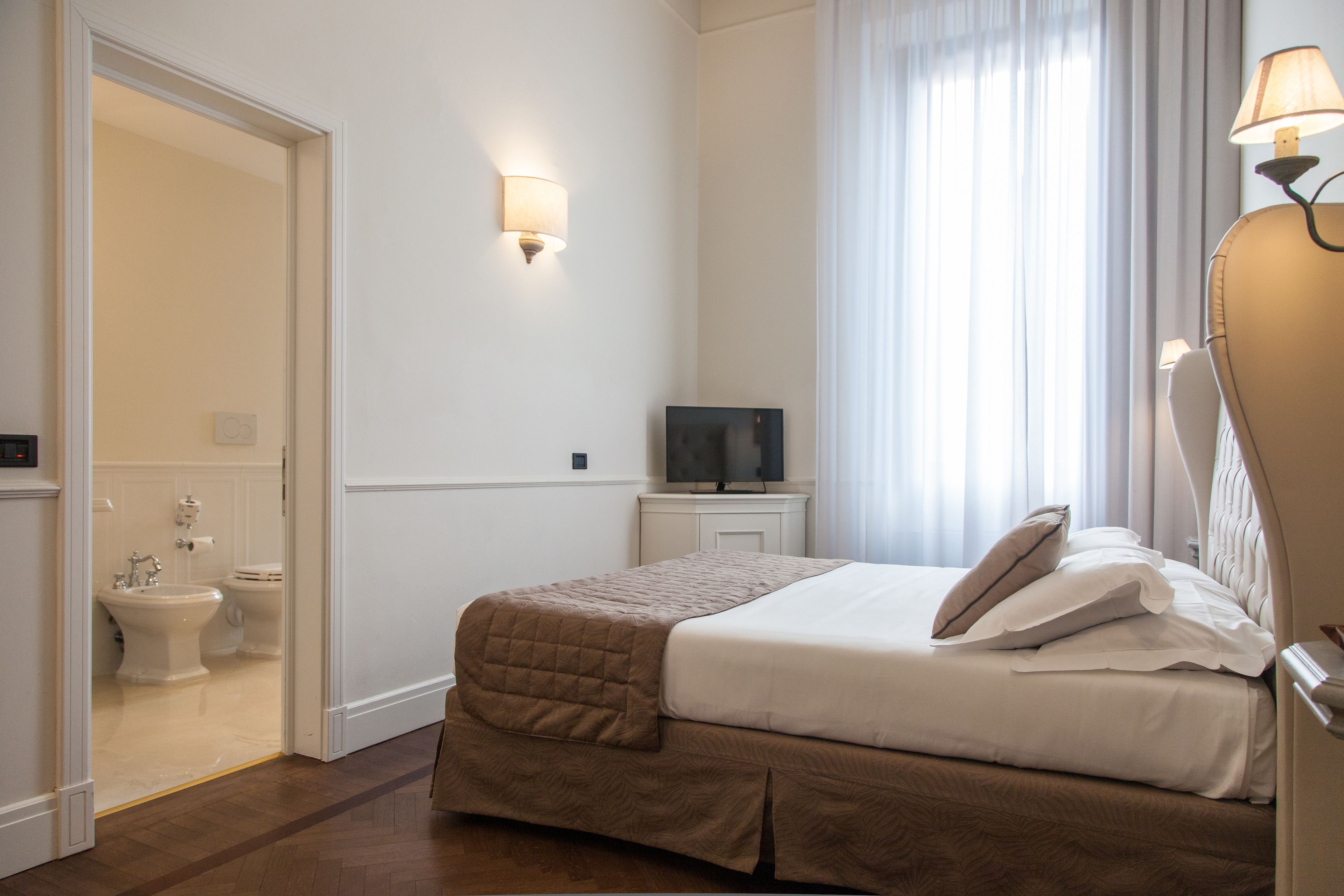 A hotel room with a bed, a television on a nightstand, a mirror, and a bathroom visible through an open door.