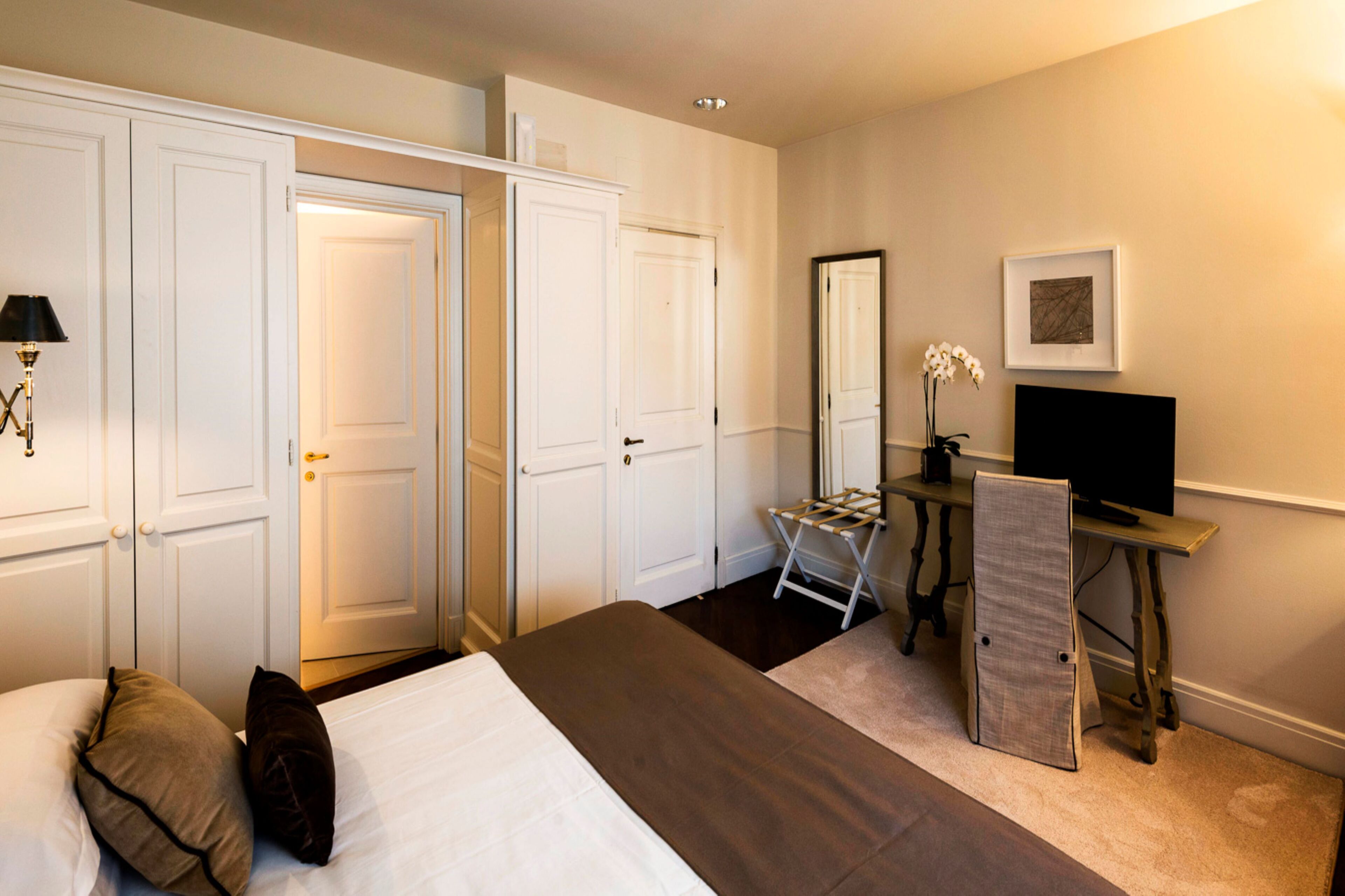 A hotel room with a bed, a desk with a chair, a television, and a wardrobe.