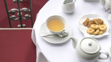 Un tavolo rotondo con una tovaglia bianca, una teiera, una tazza di tè, un piatto di biscotti e un piccolo libro.