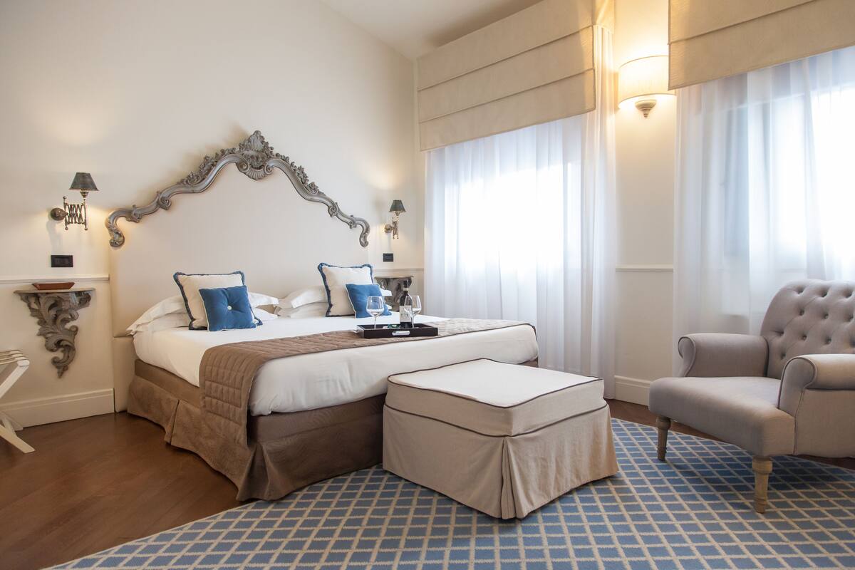Habitación de hotel con una cama grande, una silla, una mesita y una ventana con cortinas.