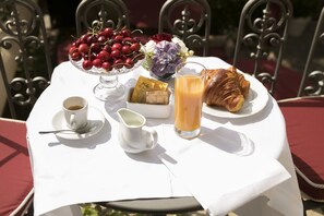 Ein Tisch gedeckt mit einer Schale Kirschen, einem Glas Orangensaft, einem Croissant, einer Tasse Kaffee und einer kleinen Zuckerdose.