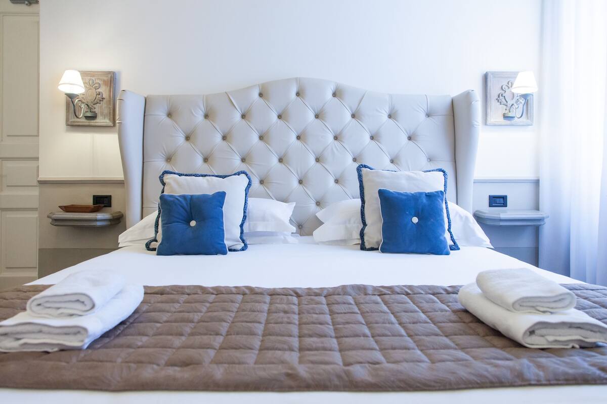 Una cama bien hecha con un cabecero capitonado, dos almohadas y un edredón doblado.