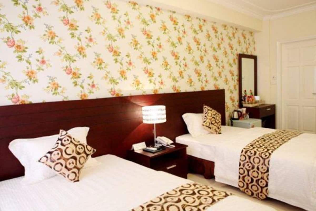 A hotel room with two beds, floral wallpaper, a wooden headboard, a bedside table with a lamp, and a mirror.