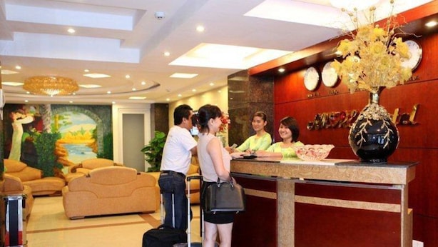 A hotel reception area with a reception desk, a mural on the wall, and a seating area with sofas. - Amore Hotel (Hanoi)