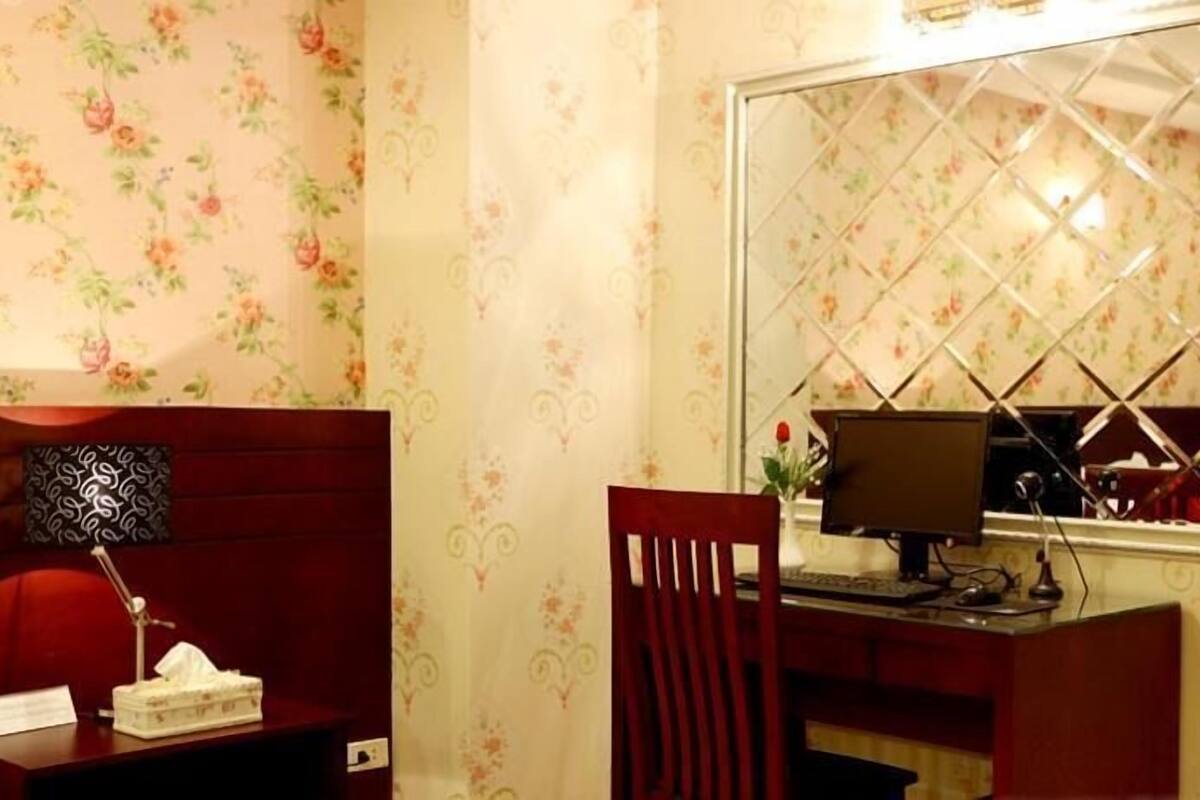 A room with floral wallpaper, a desk with a computer, a chair, and a decorative mirror.