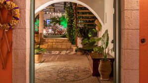 Un arco de entrada da a un espacio interior cálidamente iluminado, con suelo de piedra, vigas de madera y plantas en macetas.
