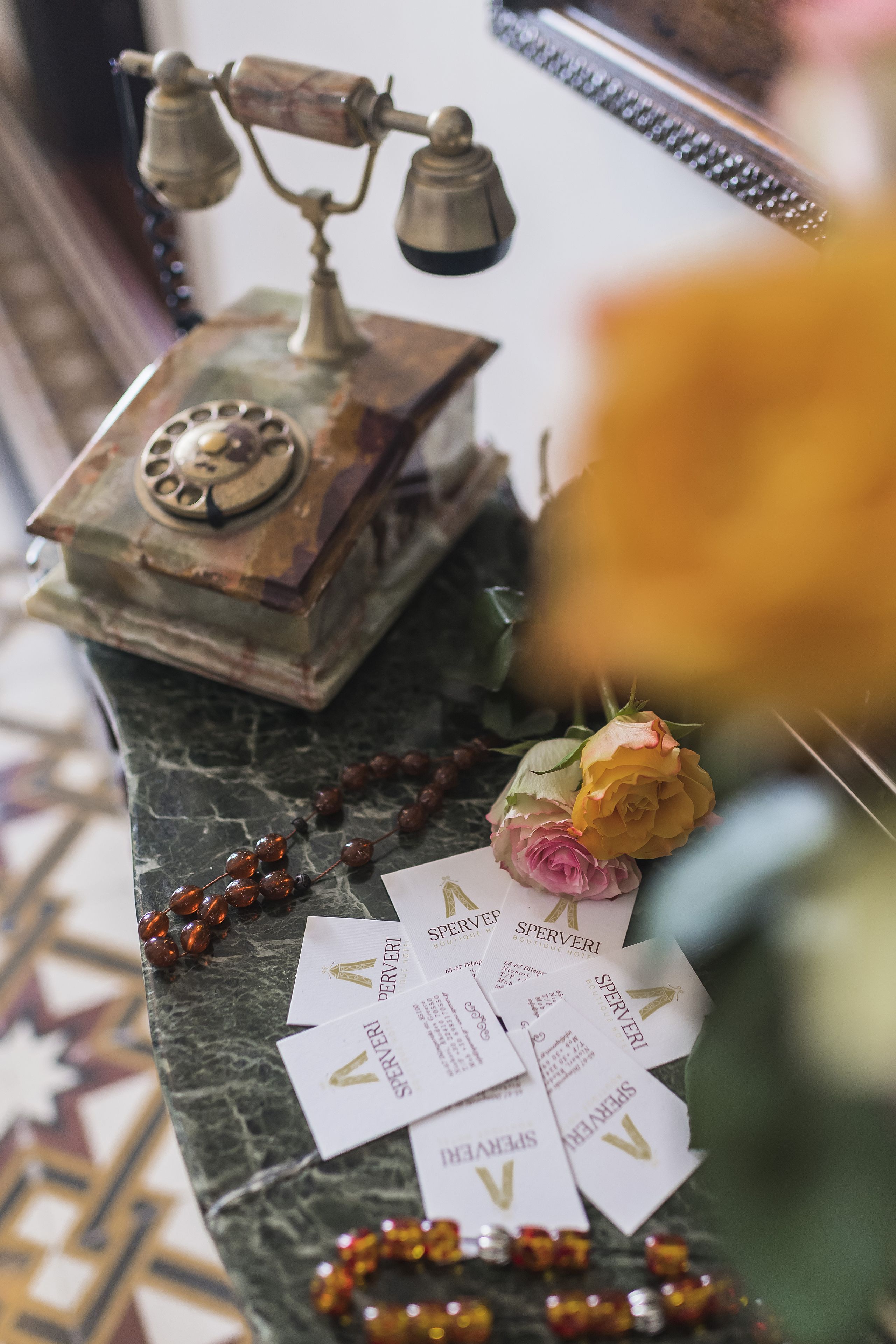 A marble table with a vintage rotary phone, a rosary, and business cards.