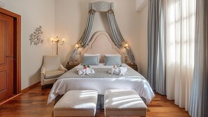 Un dormitorio ordenado con una cama grande, dos mesitas de noche, una silla y un dosel.