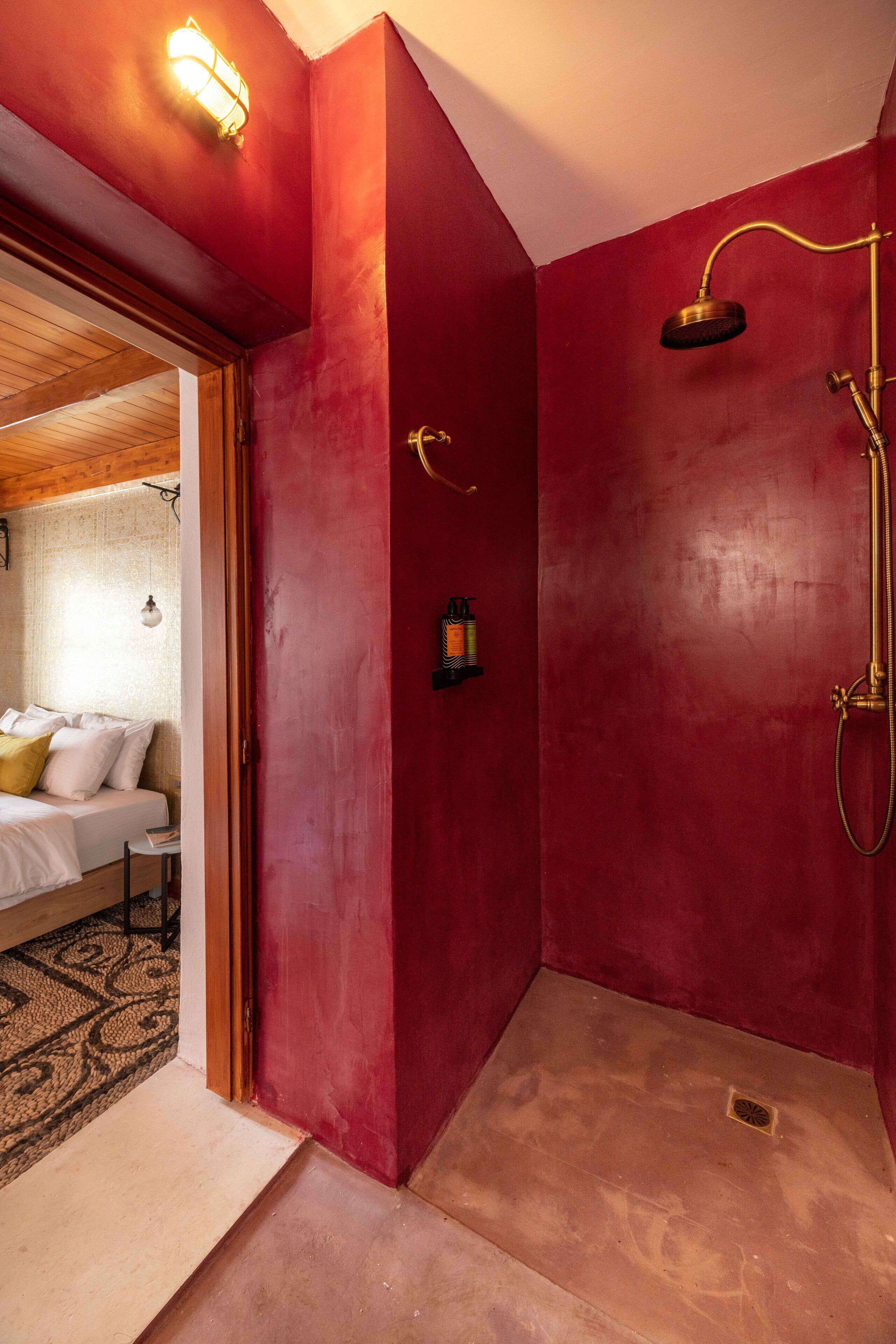A red-walled bathroom with a shower, a small shelf, and a light fixture.