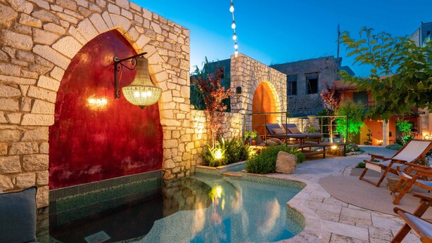 Zona de piscina con paredes de piedra, sillones de descanso y un edificio de piedra al fondo.