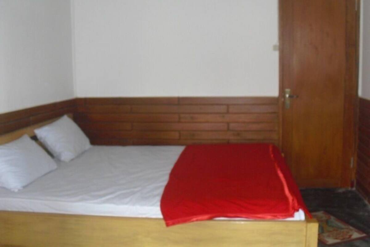 A single bed with a wooden headboard, a red blanket, and a white pillow.