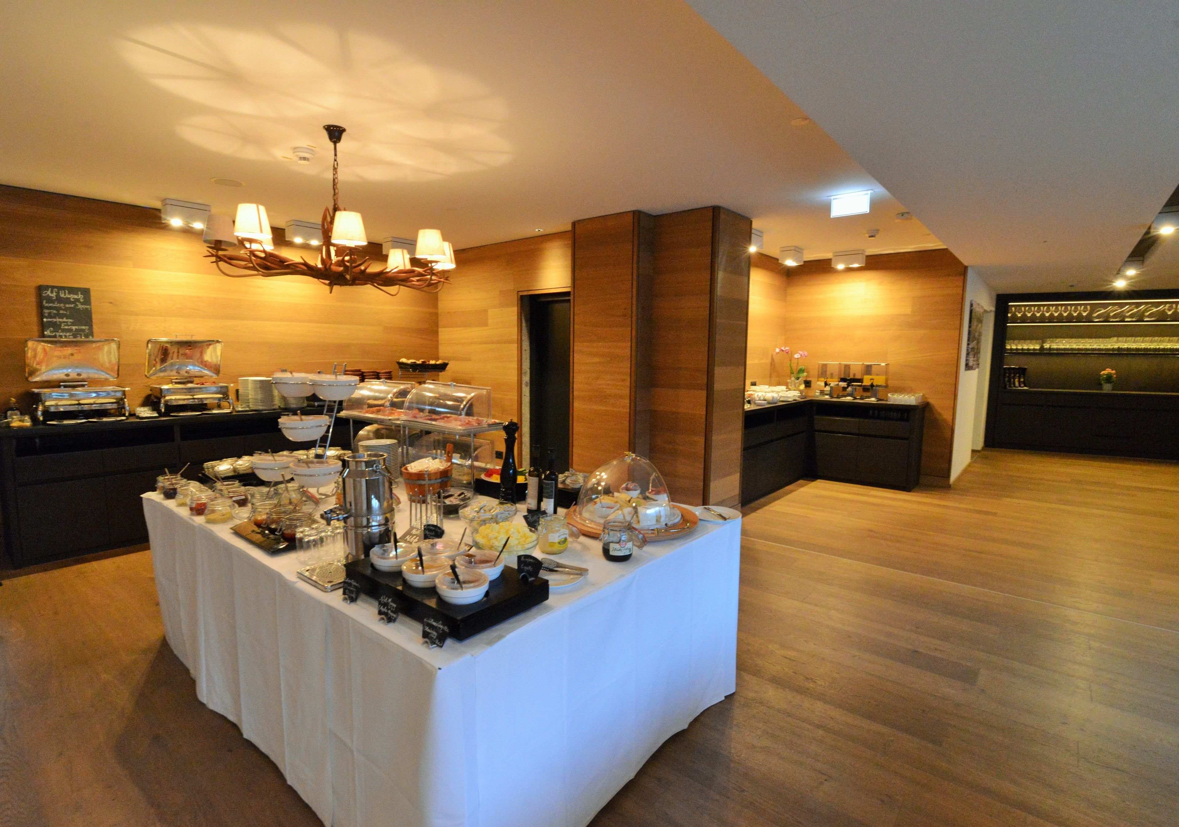 Disposição de buffet com diversos alimentos e um espaço para café, em uma sala com paredes de madeira e um candelabro.