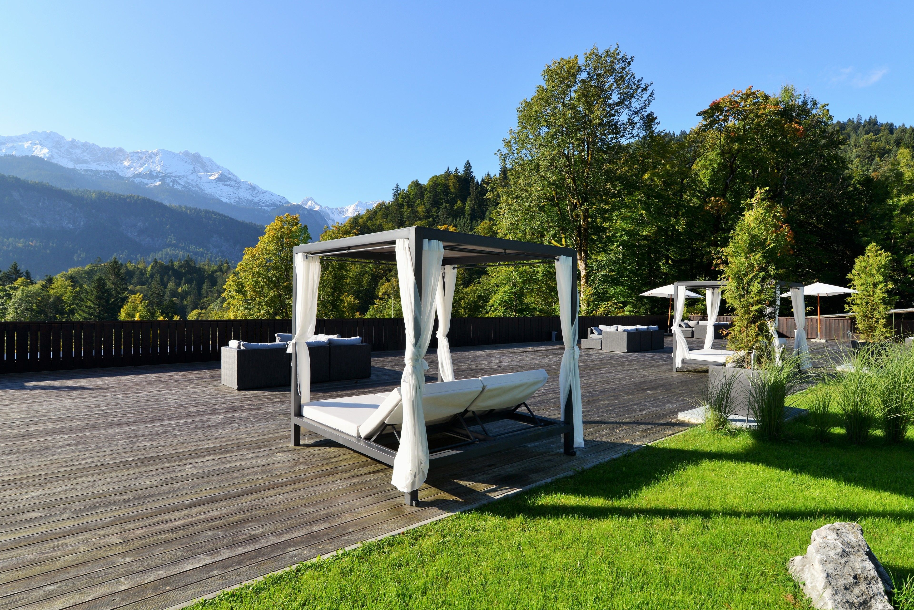 Une terrasse en bois dotée d’un lit à baldaquin, d’un espace salon extérieur et offrant une vue sur des montagnes enneigées.