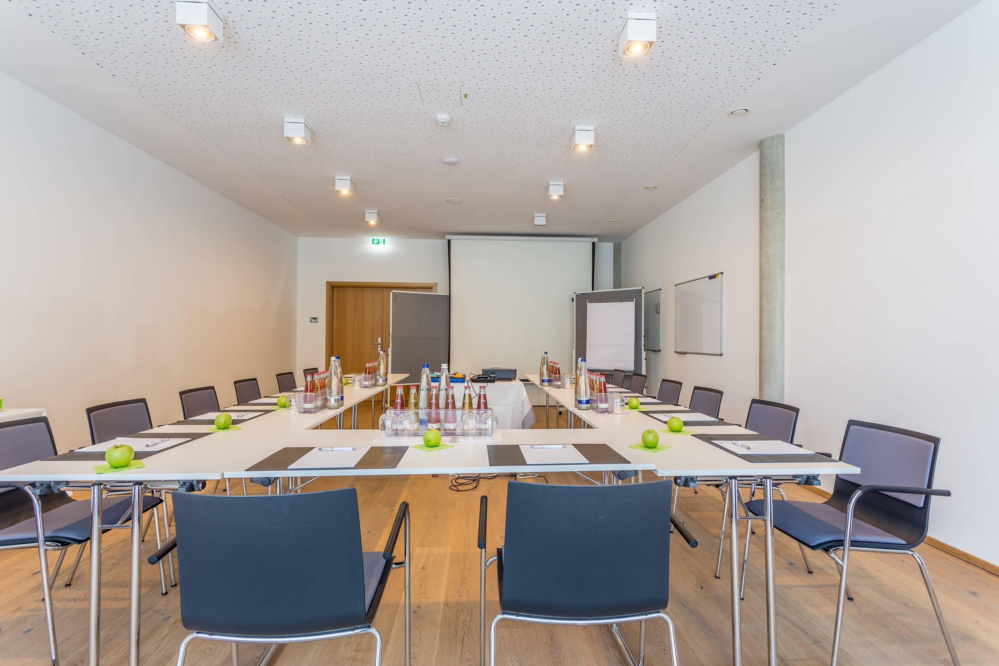 A conference room with a long table, chairs, and a projector screen.