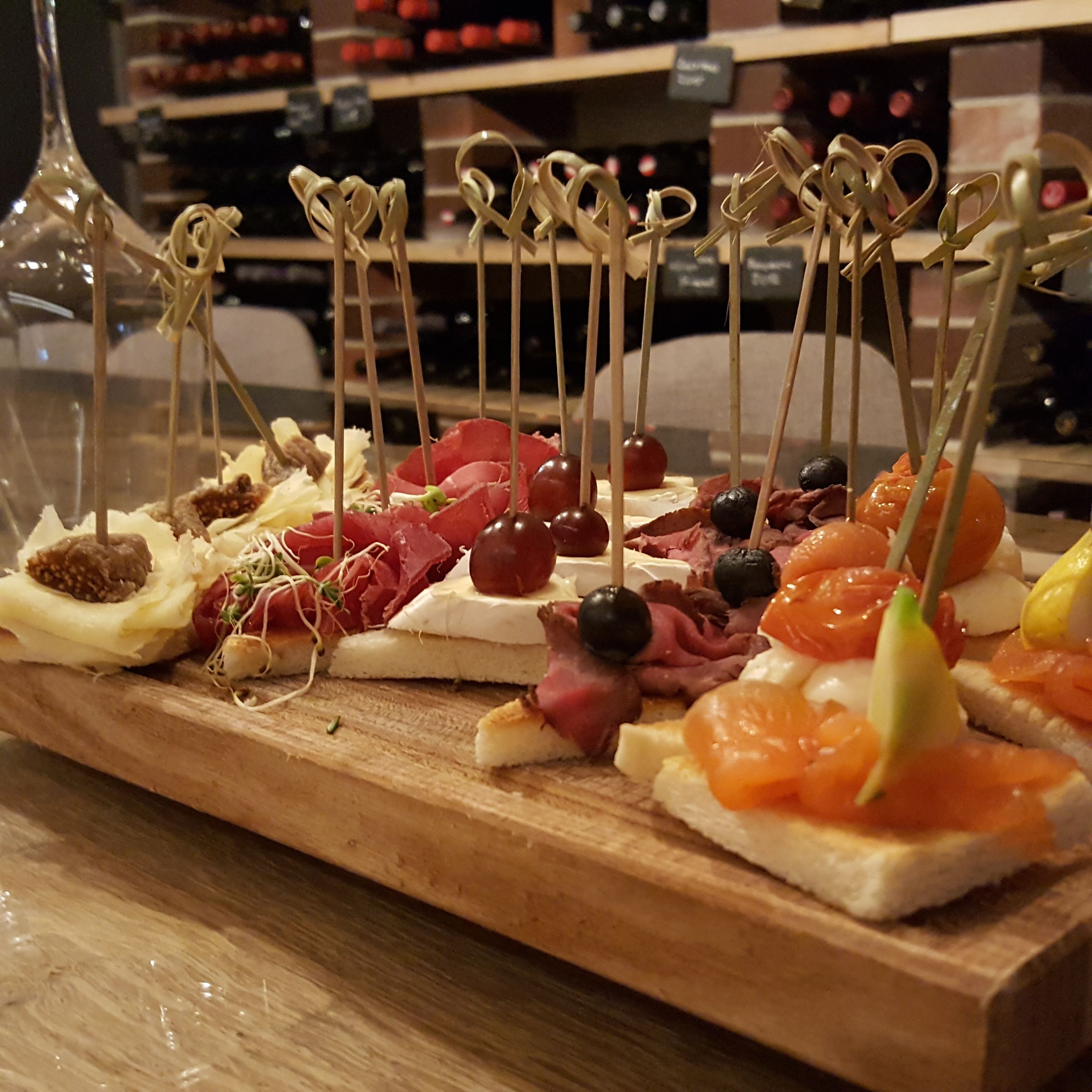 Une planche en bois sur laquelle sont disposés divers amuse-gueules, notamment des fromages, des charcuteries et des fruits, préparée pour une réception.