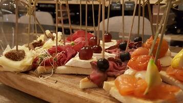 Una tabla de madera con varios aperitivos, como quesos, embutidos y frutas, dispuesta para una reunión.