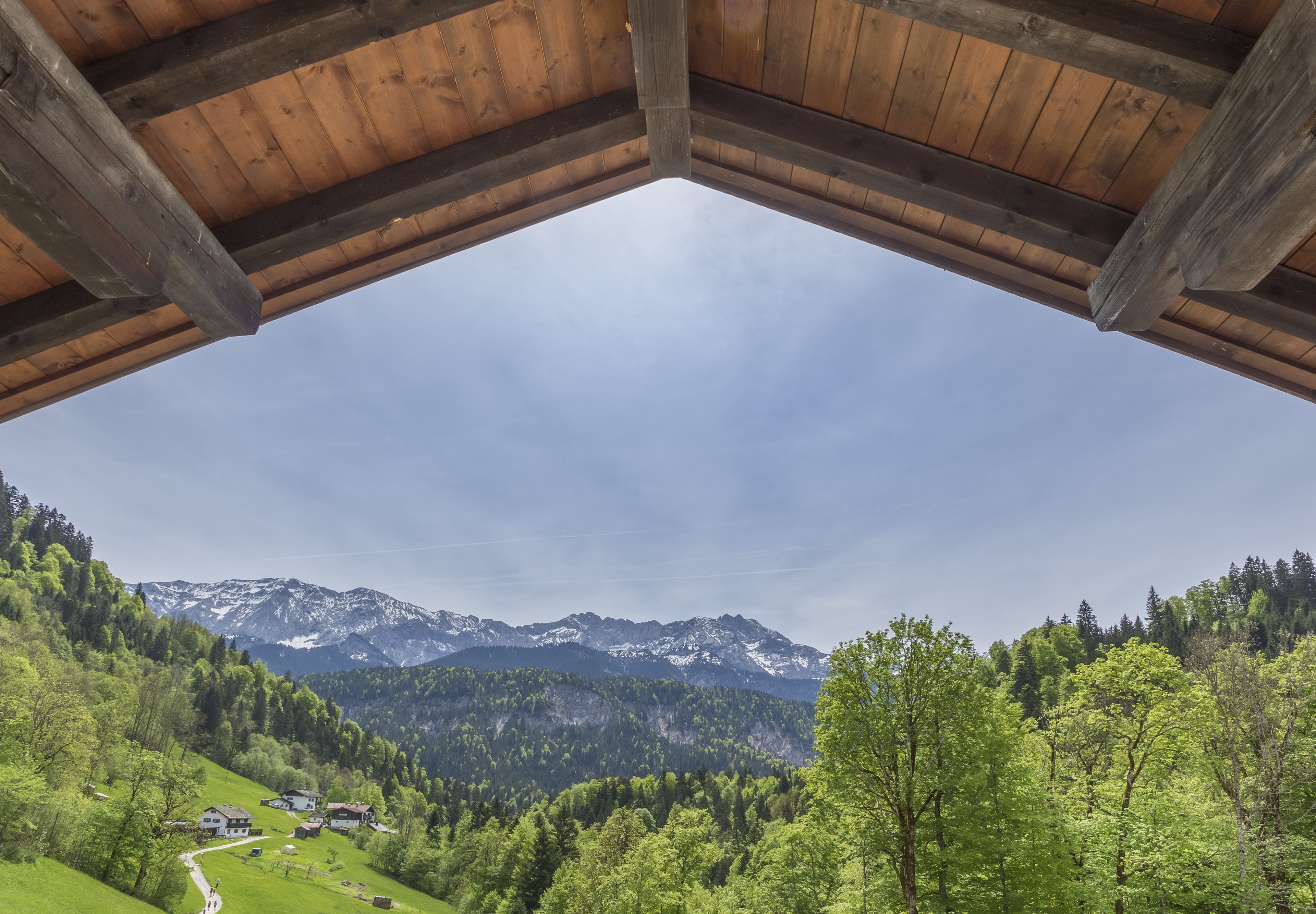 A wooden roofed structure with a view of a green valley, mountains, and a clear sky.