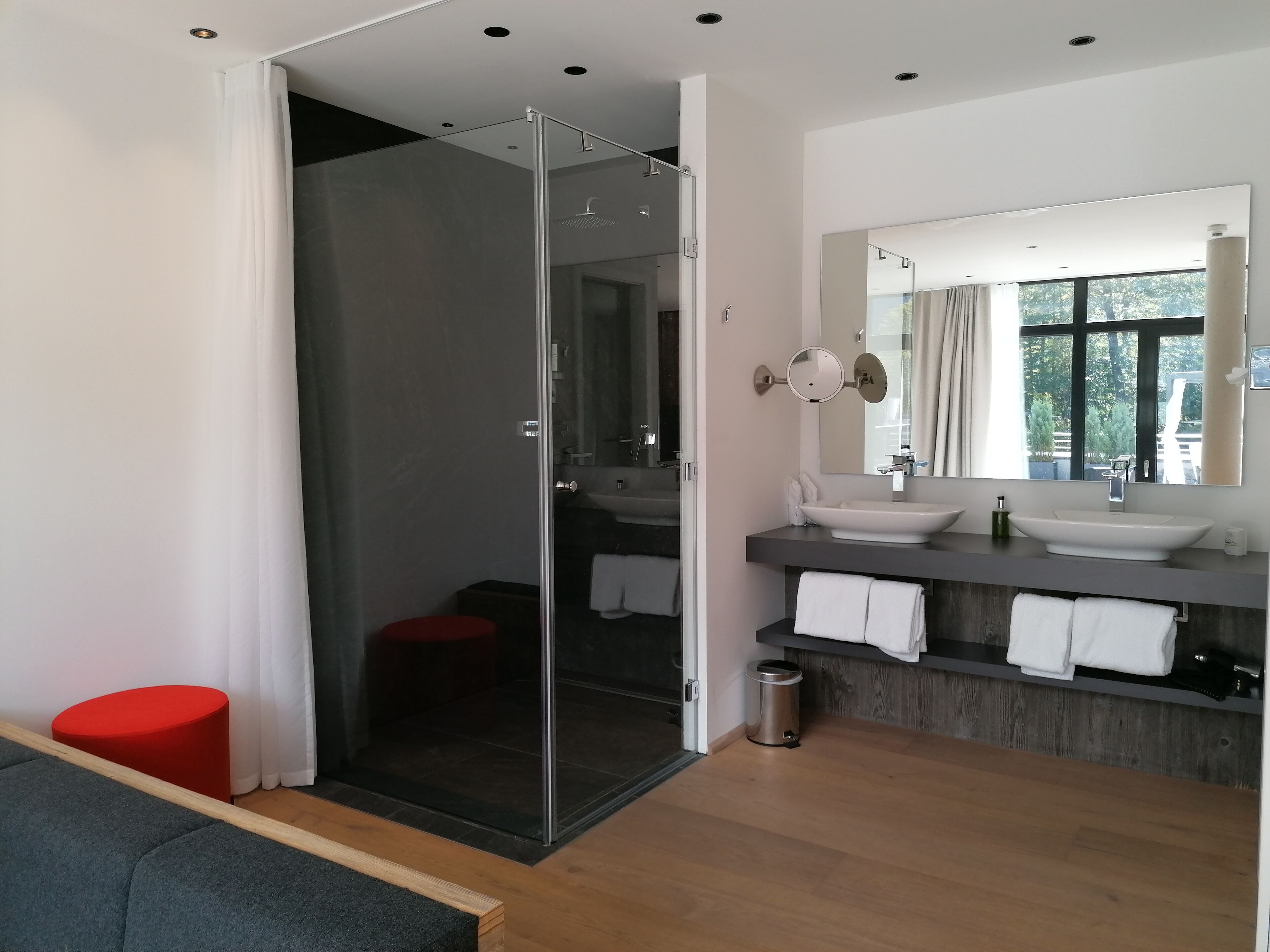 Une salle de bain moderne dotée d’une douche à parois de verre, d’un grand miroir et d’un meuble-lavabo avec un évier et un porte-serviettes.