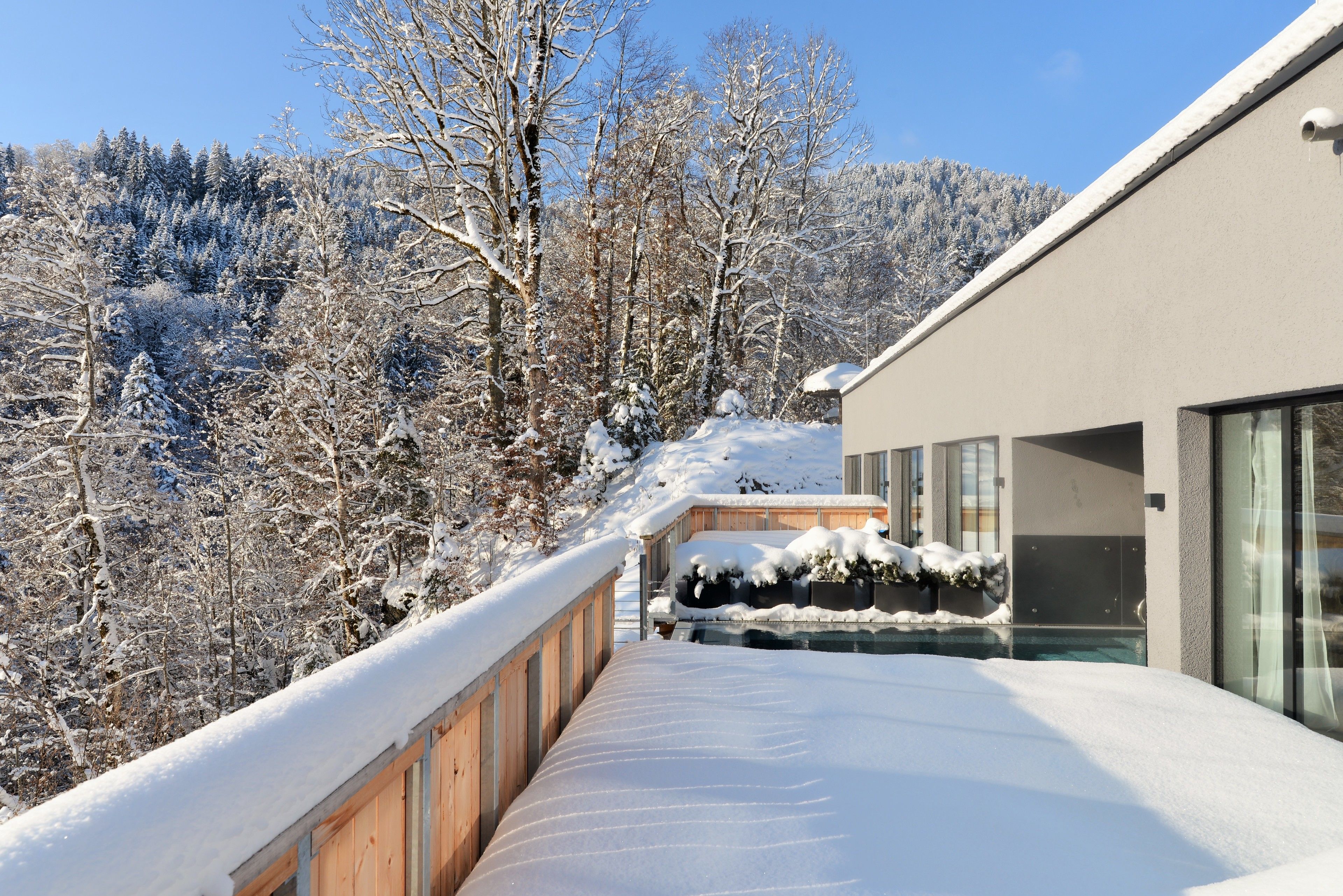 Un edificio moderno con un balcón cubierto de nieve que da a una zona boscosa.
