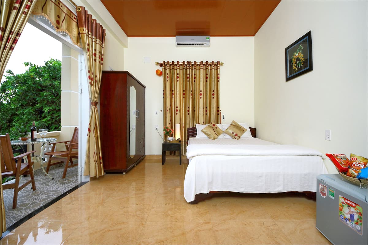 A bedroom with a bed, a desk with chairs, a wardrobe, and a suitcase.