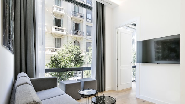 A modern living room with a grey sofa, two armchairs, a small round table, and a TV on the wall. - Murmuri Residence Mercader (Barcelona)