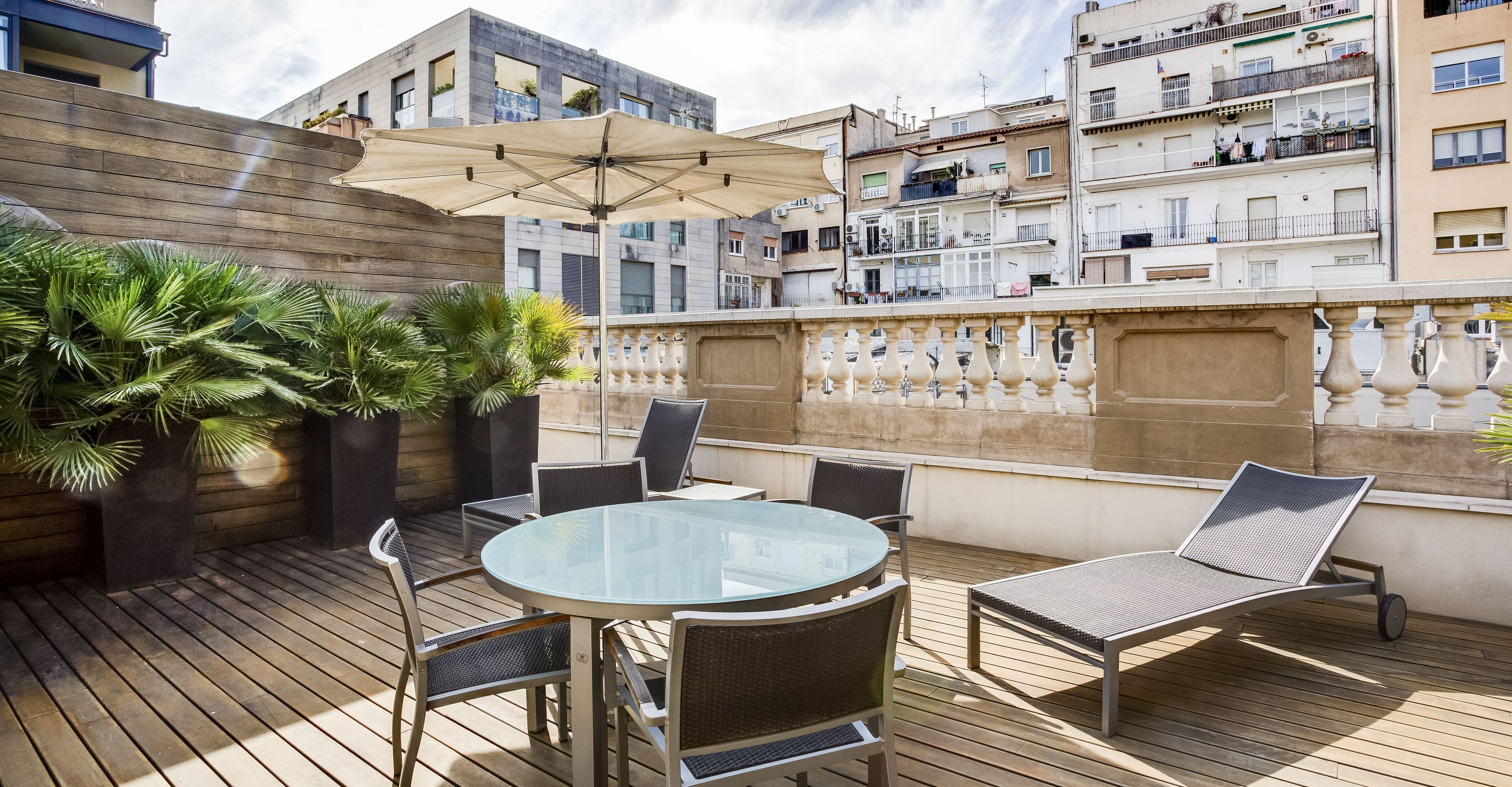 Una terraza en la azotea con una mesa de vidrio, sillas y una tumbona.