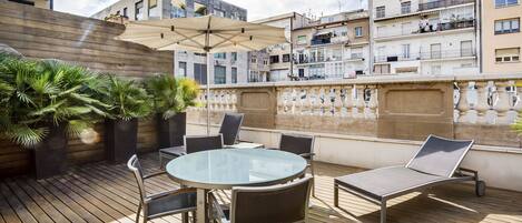 Una terraza en la azotea con una mesa de vidrio, sillas y una tumbona.