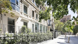 A row of classic townhouses with large windows, a metal fence, and a tree-lined street. - Murmuri Residence Mercader (Barcelona)