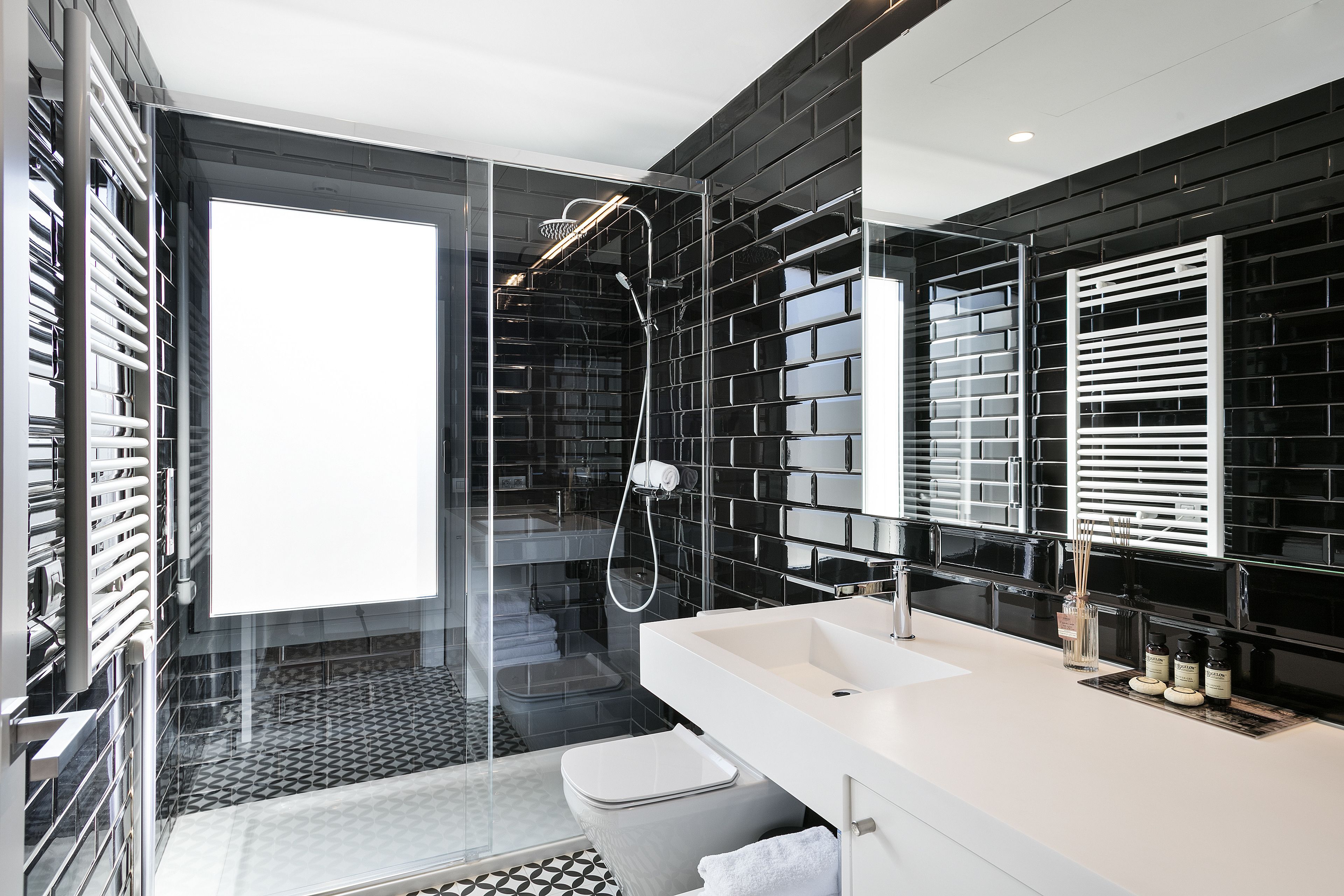 Un baño moderno con ducha de vidrio, lavamanos blanco y paredes con azulejos negros.
