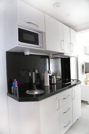 A modern kitchen with white cabinetry, a black countertop, a microwave, a kettle, and a coffee maker. - Ditto Flats (Istanbul)
