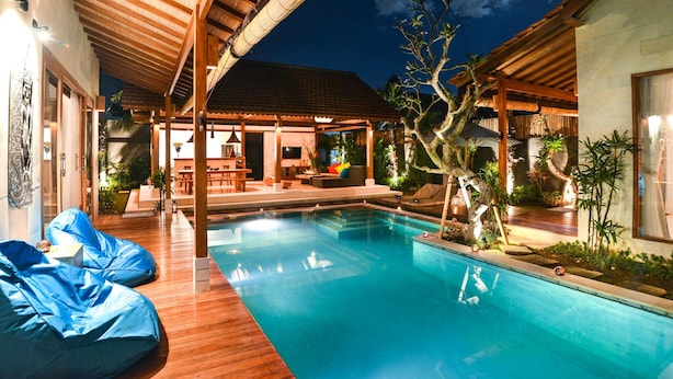 Piscina con cubierta de madera, zona de estar techada y espacio exterior bien iluminado con plantas.