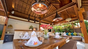 Un comedor de madera con techo alto, iluminación colgante y vista a la vegetación exuberante.
