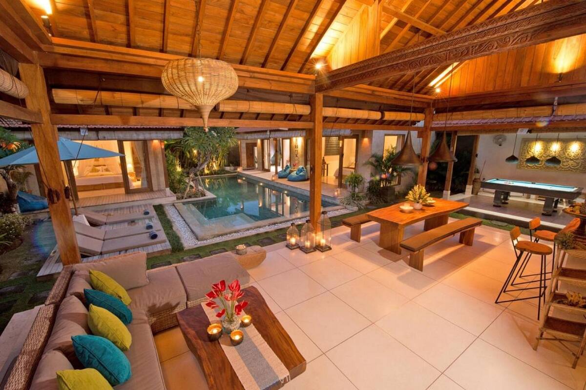 Un patio exterior con piscina, mobiliario de madera y zona de bar.