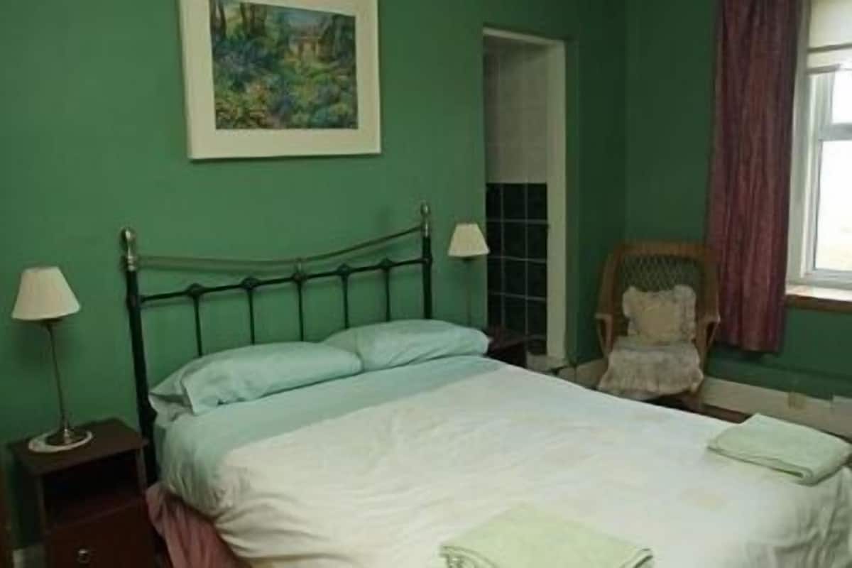 A bedroom with a bed, a chair, a painting, and a window.
