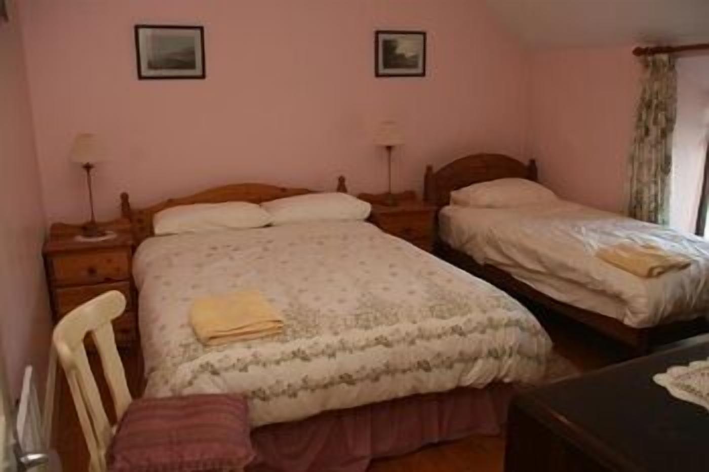 A bedroom with two single beds, a wooden nightstand, a chair, and a desk.