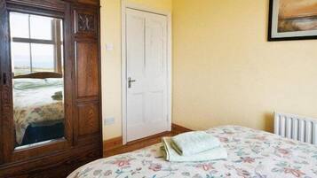 Een slaapkamer met een houten garderobe, een witte deur, een bed met een bloemenprint sprei en een schilderij aan de muur.