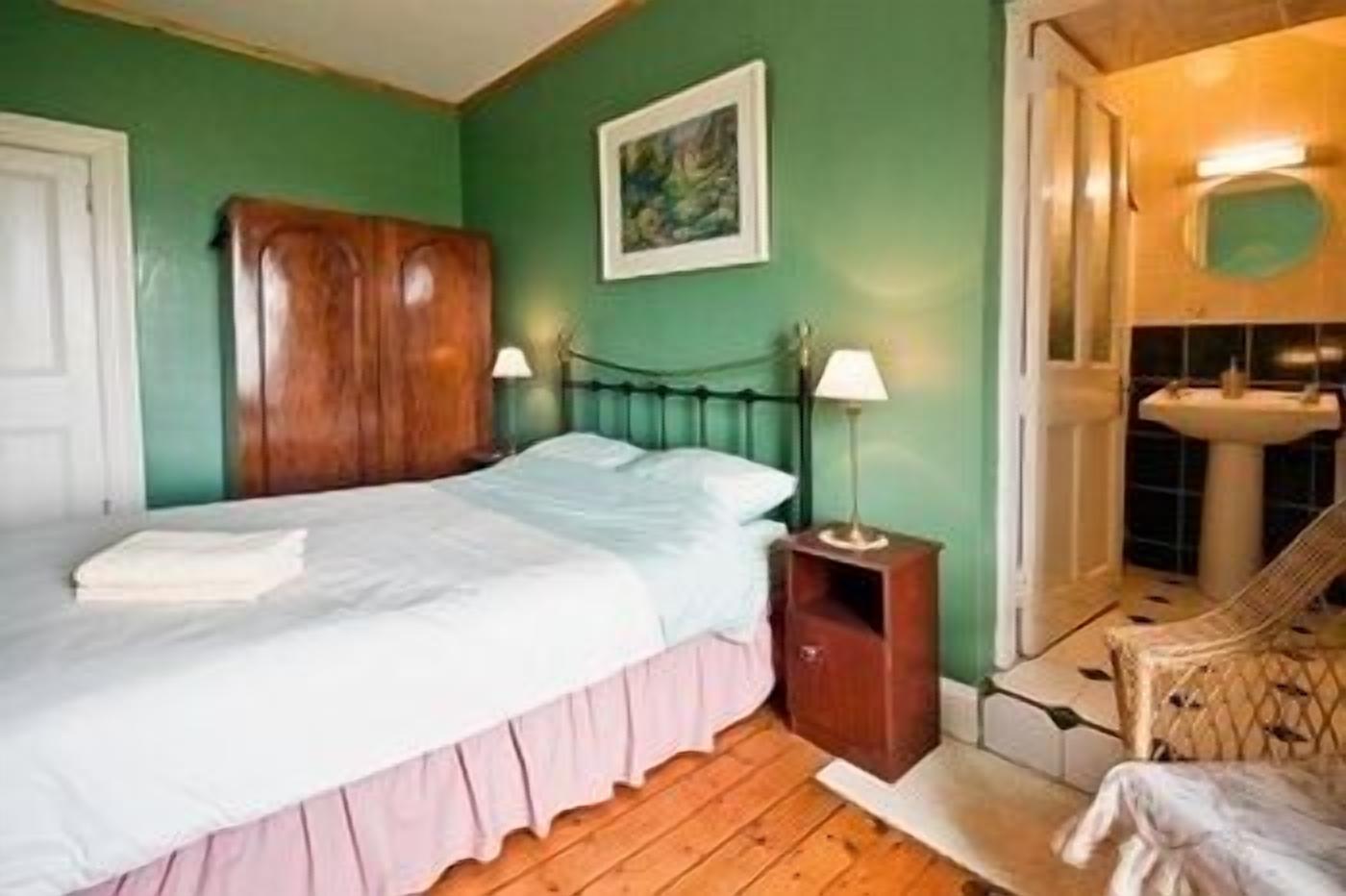 Camera da letto con un letto, comodino, lampada, armadio in legno e bagno con lavandino e doccia.