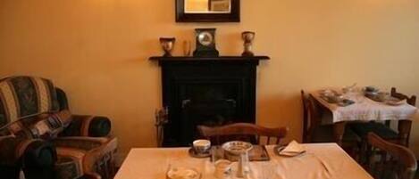 Un comedor con una mesa preparada para dos personas, una chimenea y un espejo en la pared.