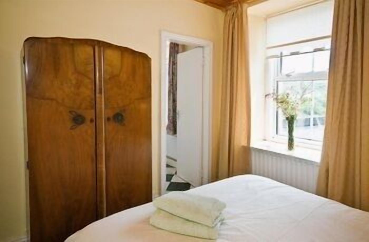 A bedroom with a bed, a wooden wardrobe, a window with curtains, and a vase with flowers.