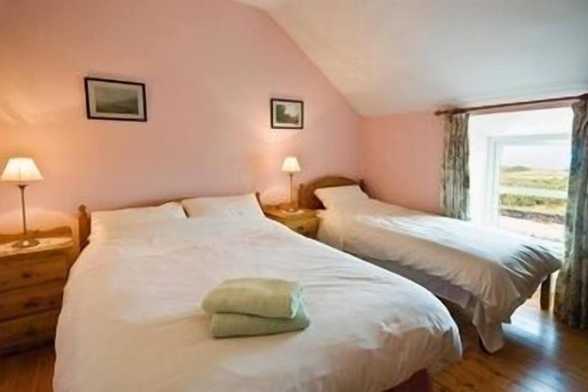 A bedroom with two beds, wooden headboards, bedside lamps, and a window with curtains.