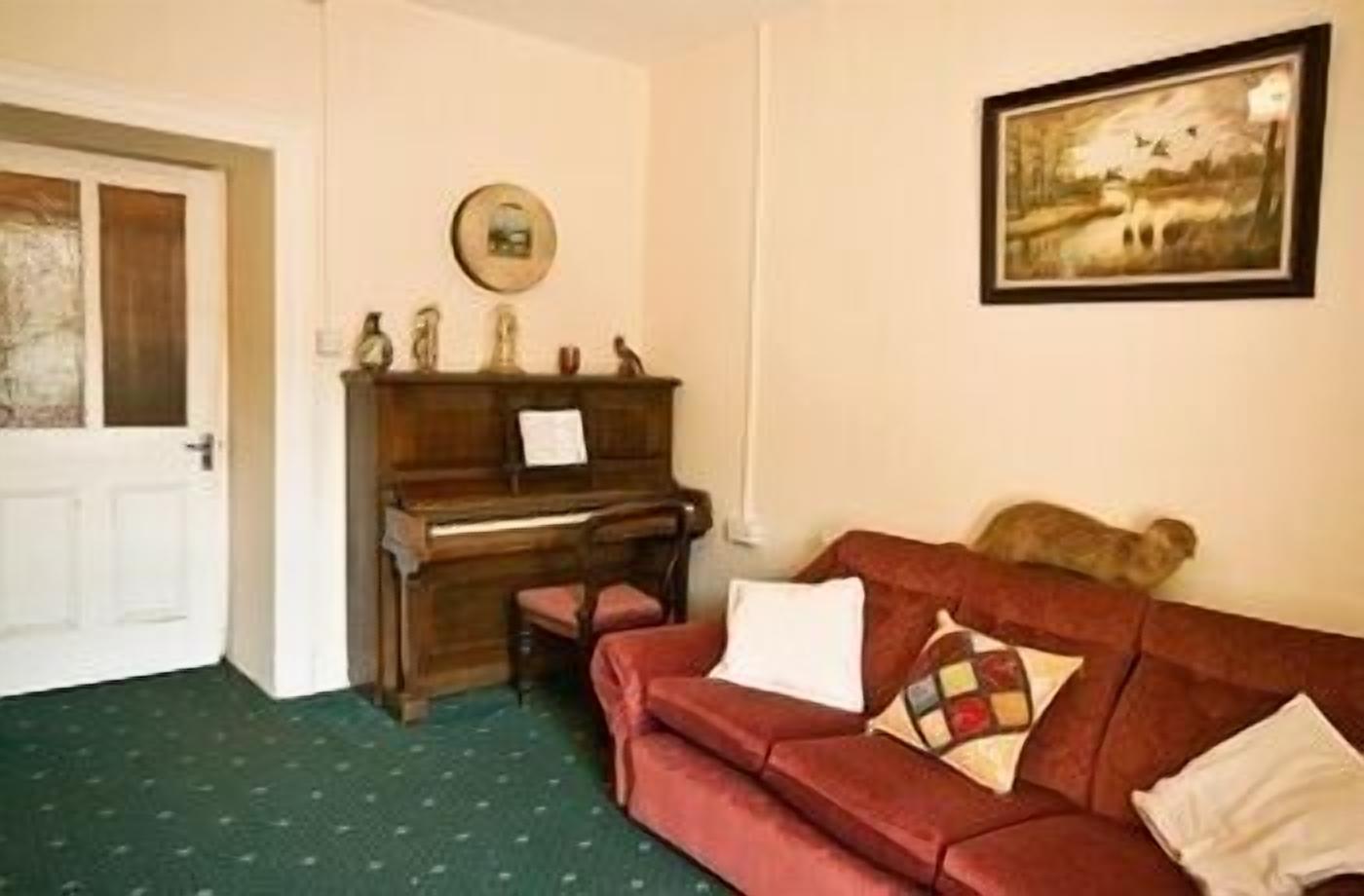 A room with a wooden piano, a red sofa with cushions, a framed picture on the wall, and a door.
