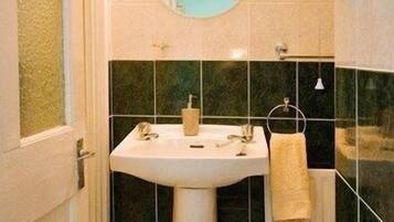 A bathroom with a pedestal sink, a round mirror, and a toilet.