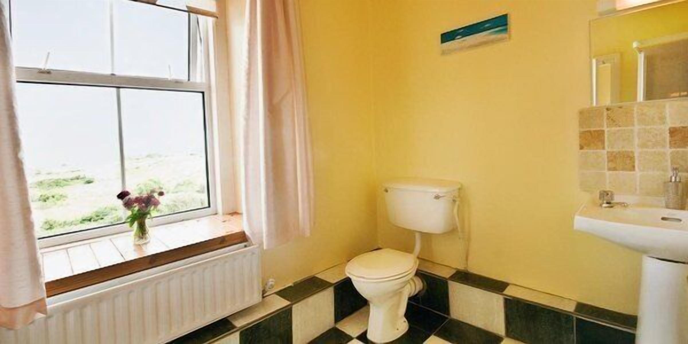 A bathroom with a toilet, sink, and window with curtains.