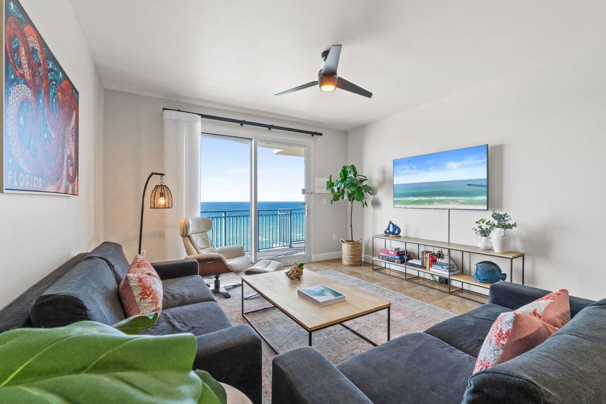 Ein geräumiges Wohnzimmer mit großem Fenster, Deckenventilator, Flachbildfernseher und Bücherregal.
